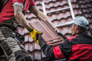 Red roof repair by two Caucasians roofers with safety equipments