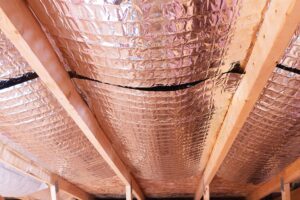 Insulating of attic with fiberglass cold barrier and reflective heat barrier 